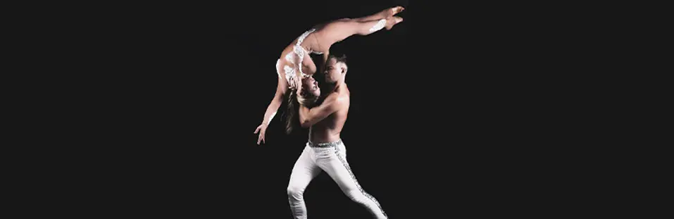 A male dancer lifting a female dancer in a dramatic pose against a dark background.